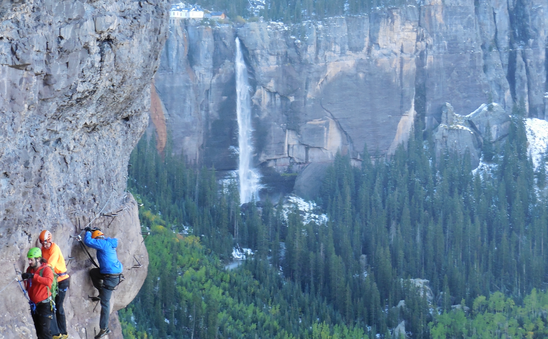Three climbers traversing the via ferrata in Telluride, Colorado with Bridal Veil Falls in the background