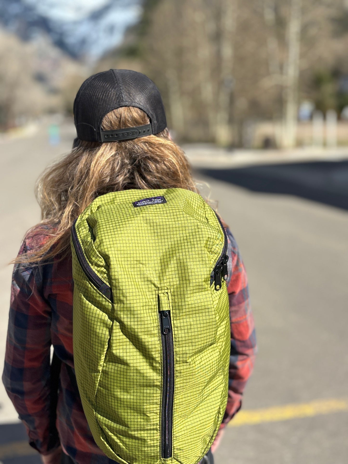 Person wearing a Jagged Edge Ajax pack with a black cap on a road with trees in the background