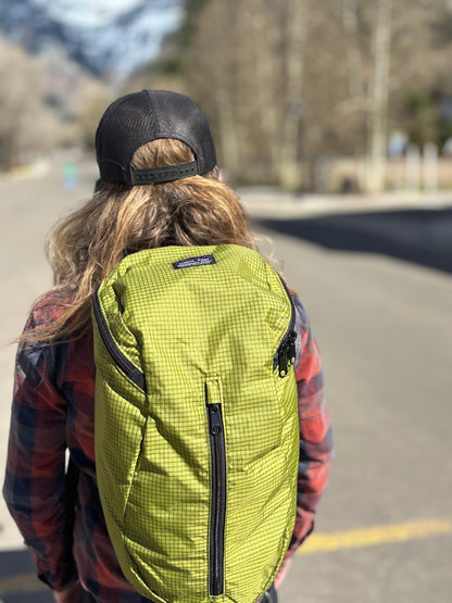 Person wearing a Jagged Edge Ajax pack with a black cap on a road with trees in the background