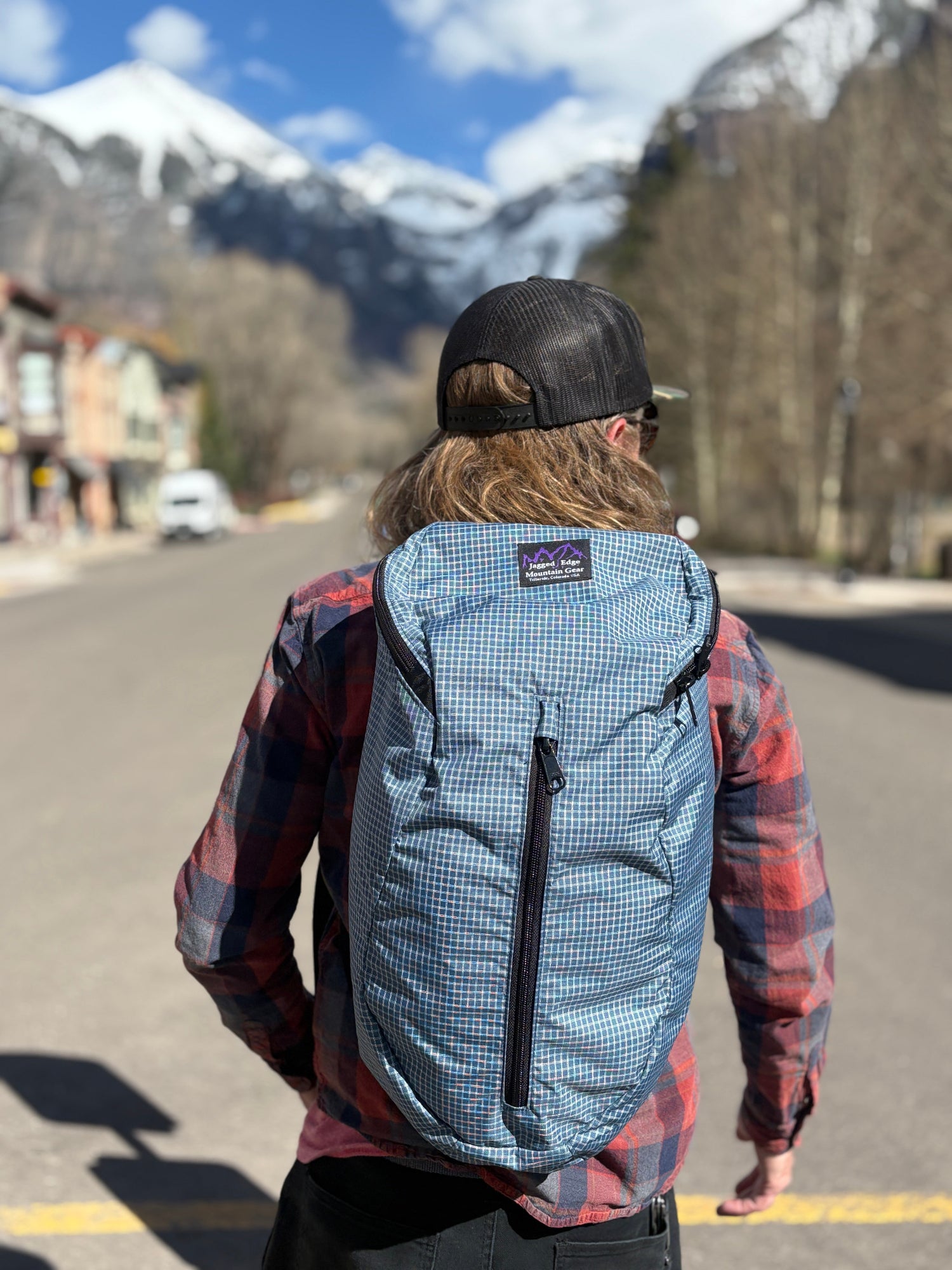 Person wearing a blue checkered Ajax Pack with mountains in the background