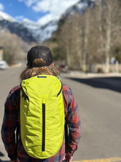 Person wearing a Jagged Edge yellow Ajax pack on a road with mountains in the background