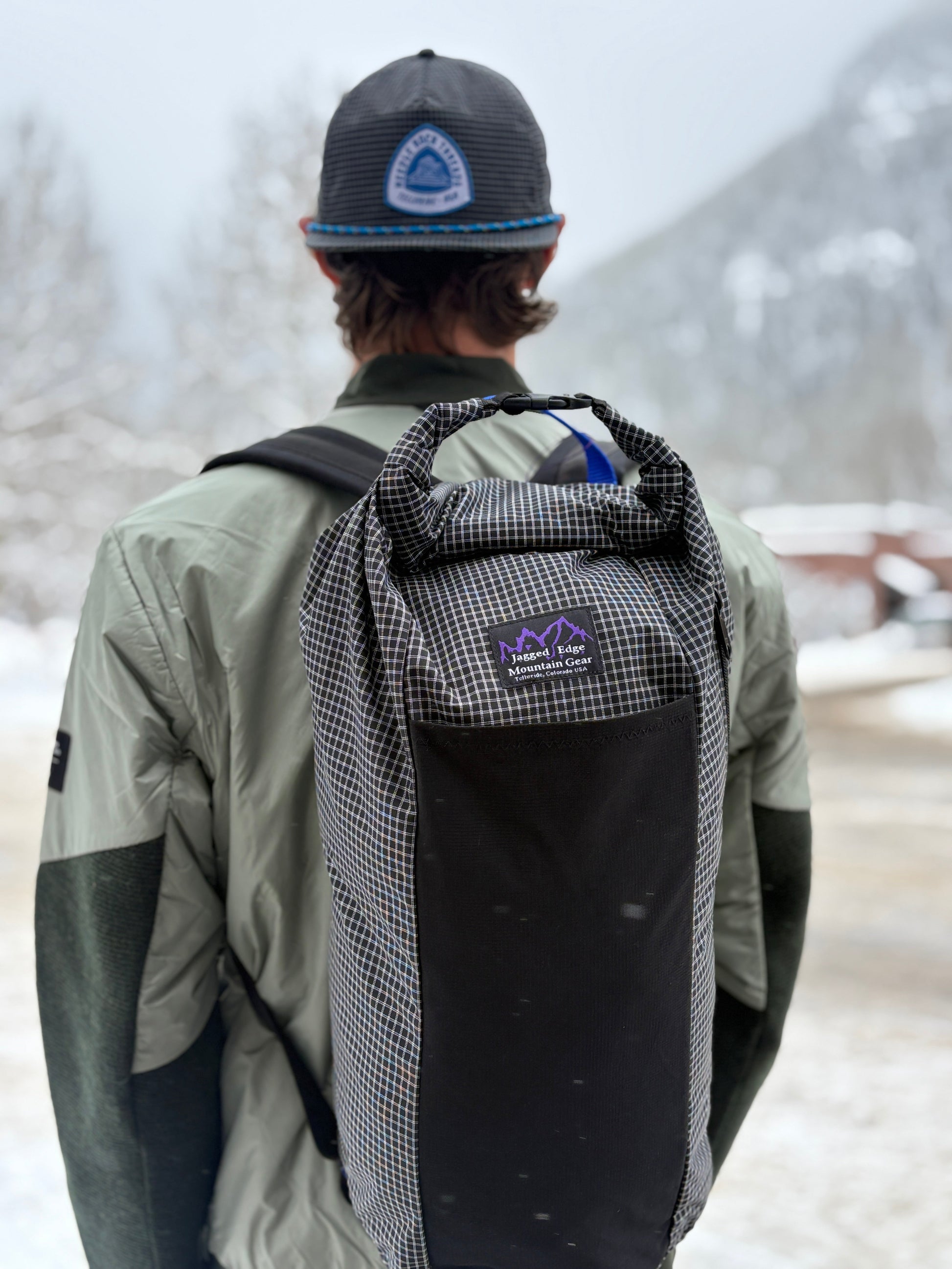 Person wearing a black and gray checkered backpack with a visible brand logo in a snowy landscape.