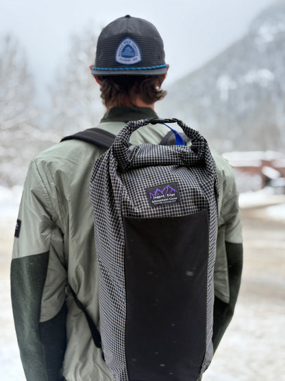 Person wearing a black and gray checkered backpack with a visible brand logo in a snowy landscape.